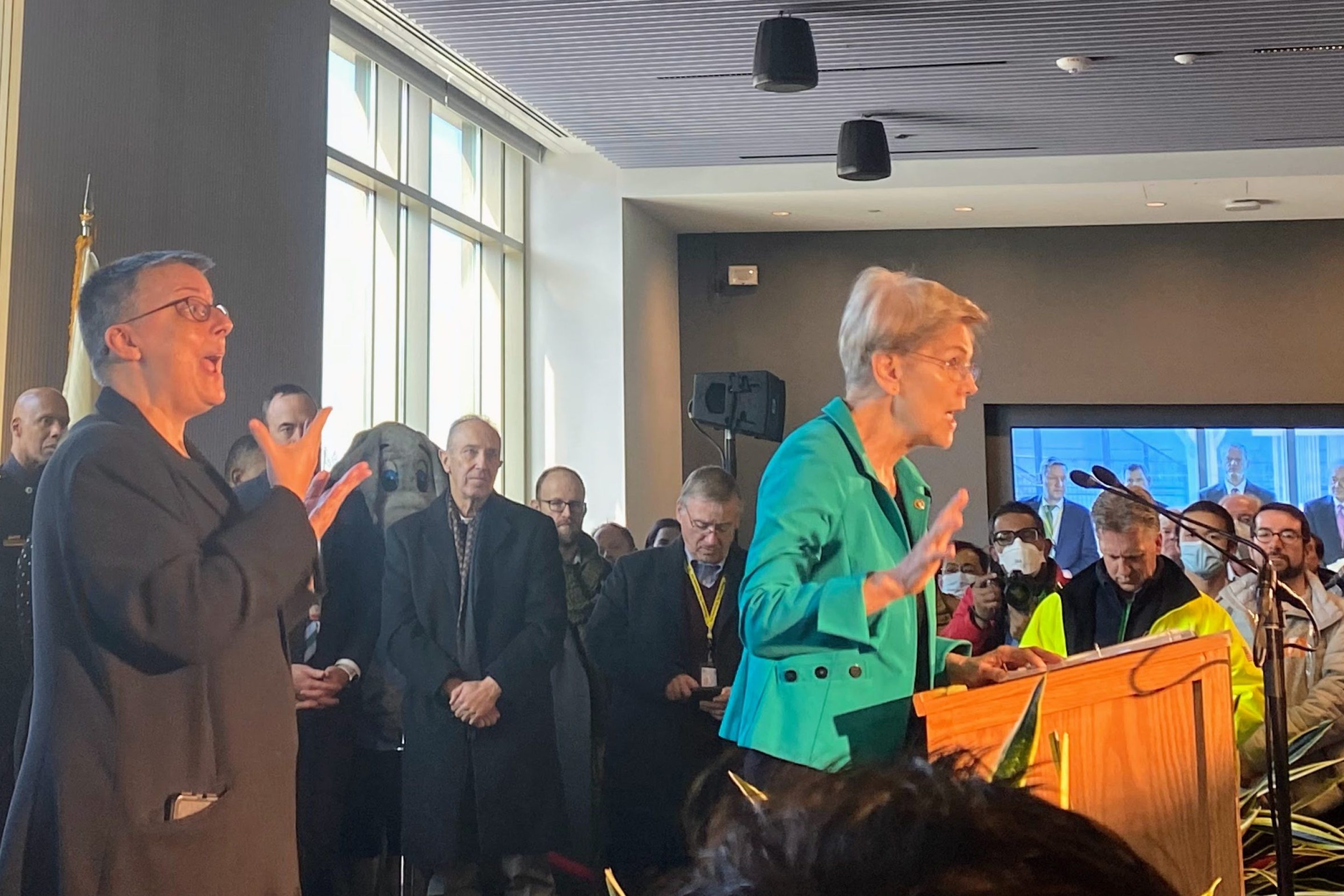 Senator Elizabeth Warren speaks to a large crowd at Tufts University. Governor Charlie Baker, Senator Ed Markey, among others, stand behind her.