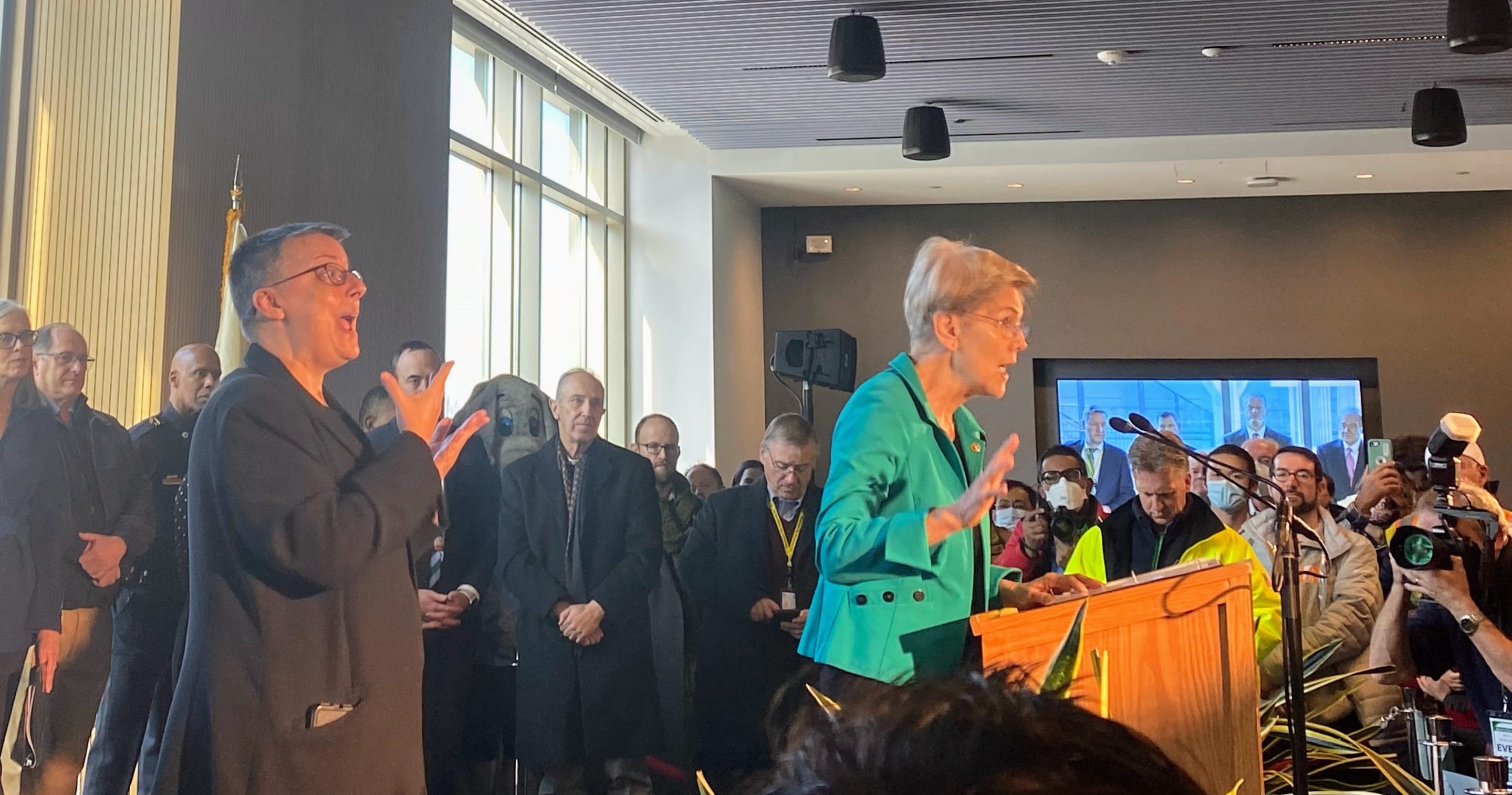 Senator Elizabeth Warren speaks to a large crowd at Tufts University. Governor Charlie Baker, Senator Ed Markey, among others, stand behind her.