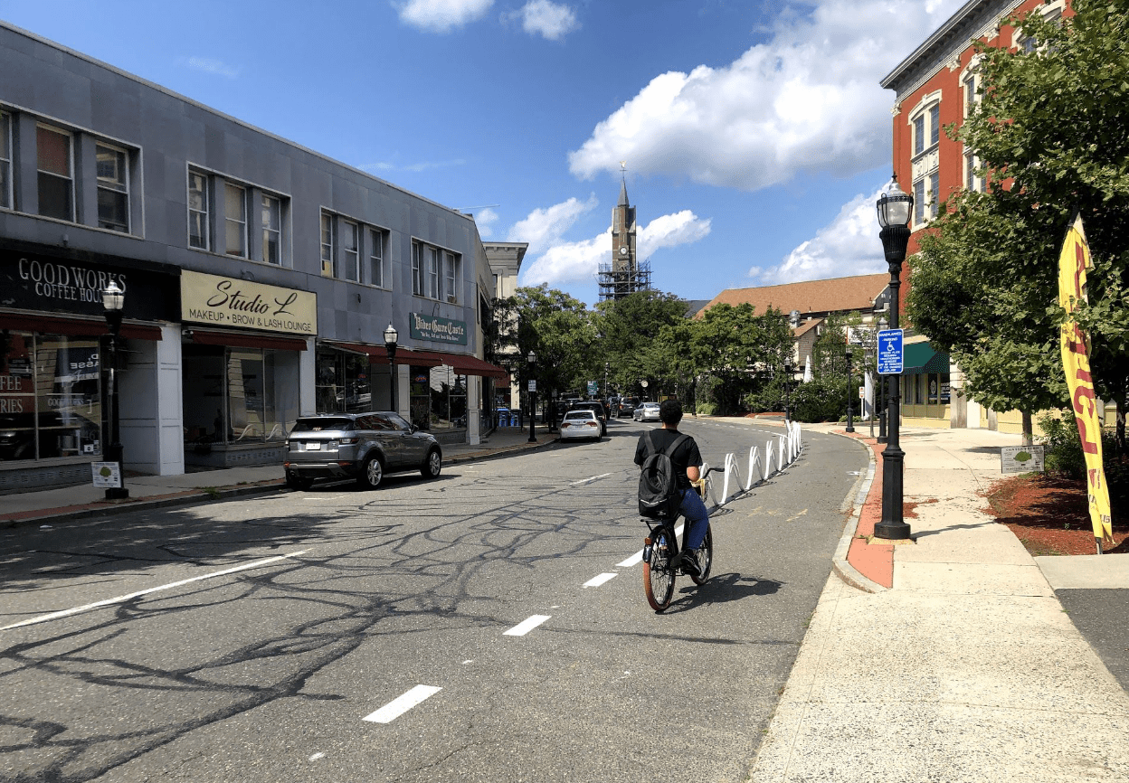 A person riding a bike along a sunny one-way street next to some two-story buildings with stores on the ground floor.