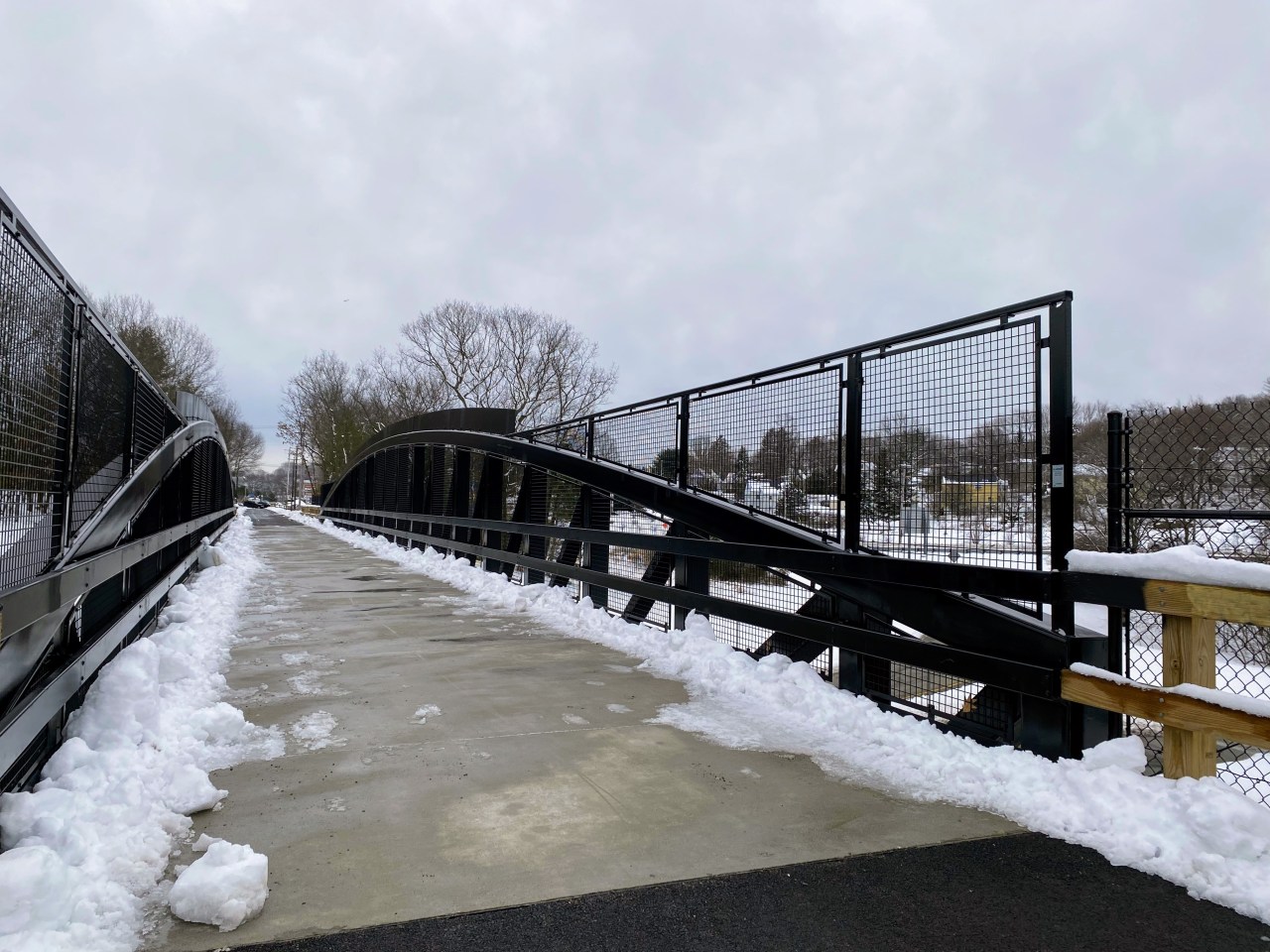 A mostly snow-cleared bridge with black metal guards to prevent people from falling.