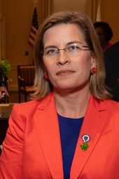 A brown-haired white woman with glasses, wearing a red blazer
