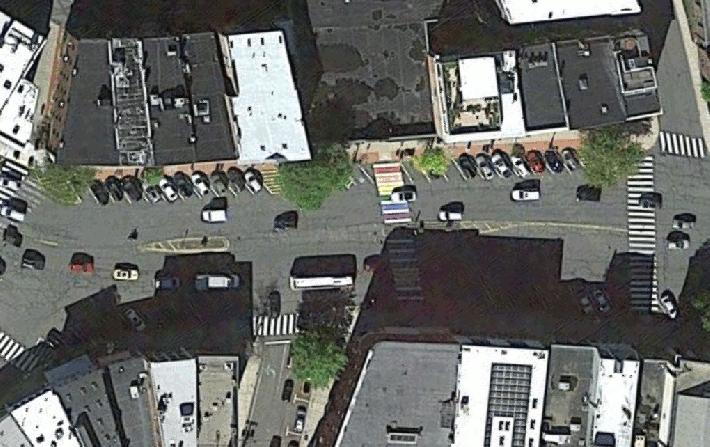 An animated GIF shows an overhead view of Northampton's Main Street between Crafts Avenue and Center Street. One frame of the animation shows the current satellite view, and the next shows the same view overlaid by MassDOT's design drawings for an upcoming construction project that will widen sidewalks, reconfigure on-street parking, and add protected bike lanes with a narrowed roadway for motor vehicles.