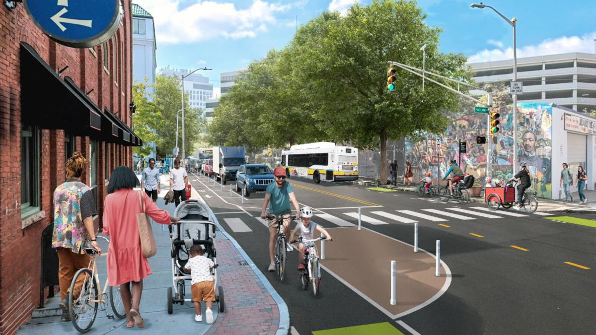 A photo-illustration rendering shows families with strollers on the sidewalk on the left, a parent and child riding bikes through a crosswalk in a bike lane next to a tan-painted island, and an MBTA bus in the distance.