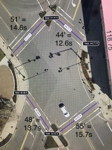 An overhead view of a wide, X-shaped intersection, with measurements of each of the four crosswalks on each leg. The Main Street crosswalks, in the upper left and lower right, are 51 feet and 55 feet wide, respectively, while the cross-street crosswalks in the upper right and lower left are 44 feet and 48 feet, respectively. Two traffic signal mast arms and their shadows are visible in the center of the photo.