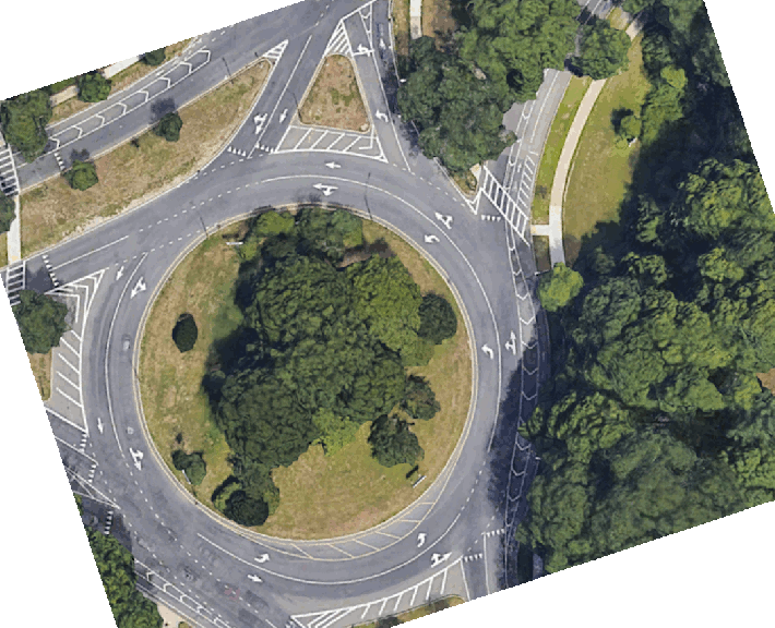 An animated GIF illustrating an aeral view of a multi-lane traffic circle with a line-drawing illustration of new striping plans for the traffic circle. The plan view shows the addition of a third traffic lane on the right (south) edge of the circle alongside the trees of the Arnold Arboretum.