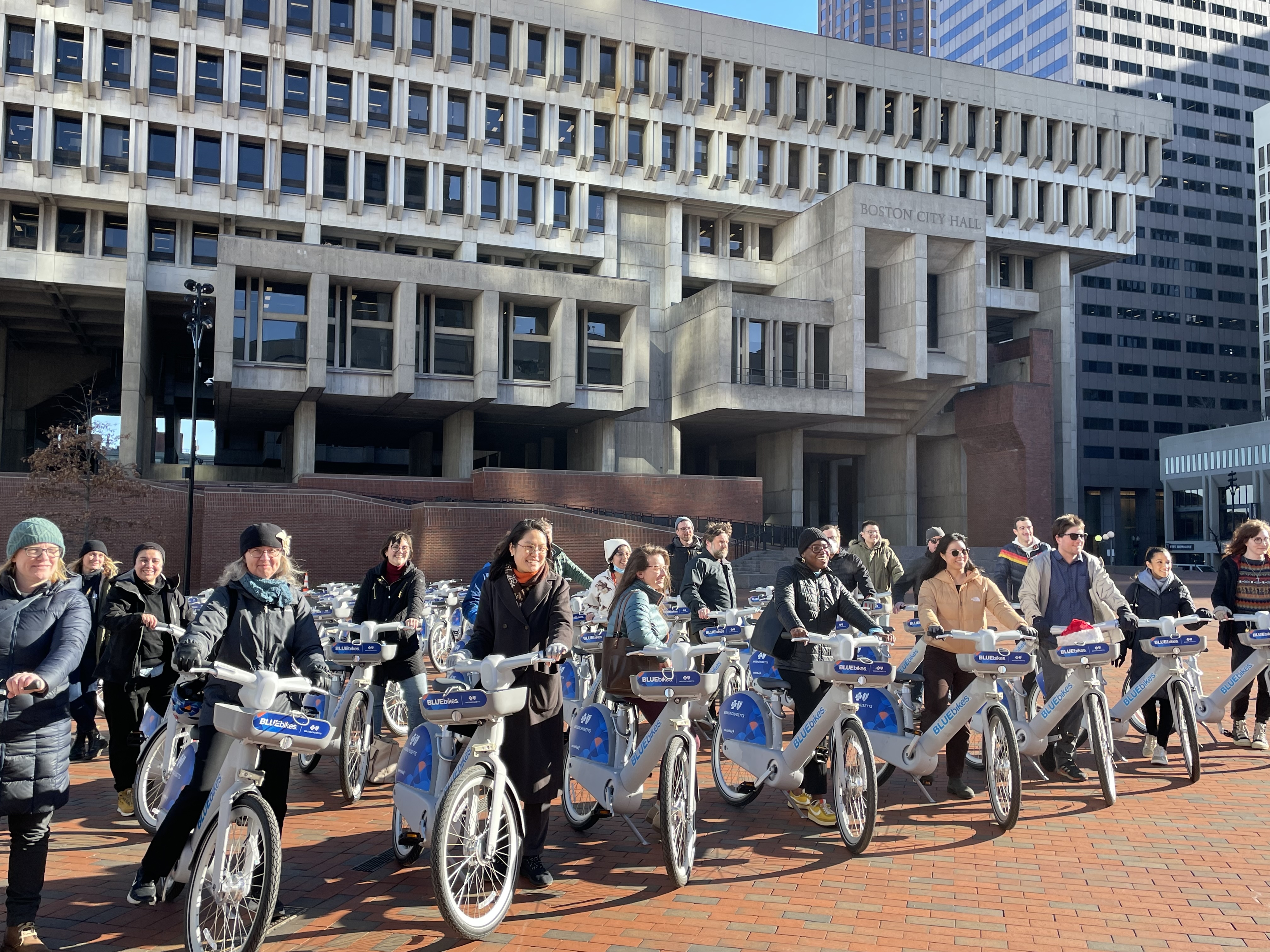 A crowd of people stand with new electric bikes in front of Boston City Hall