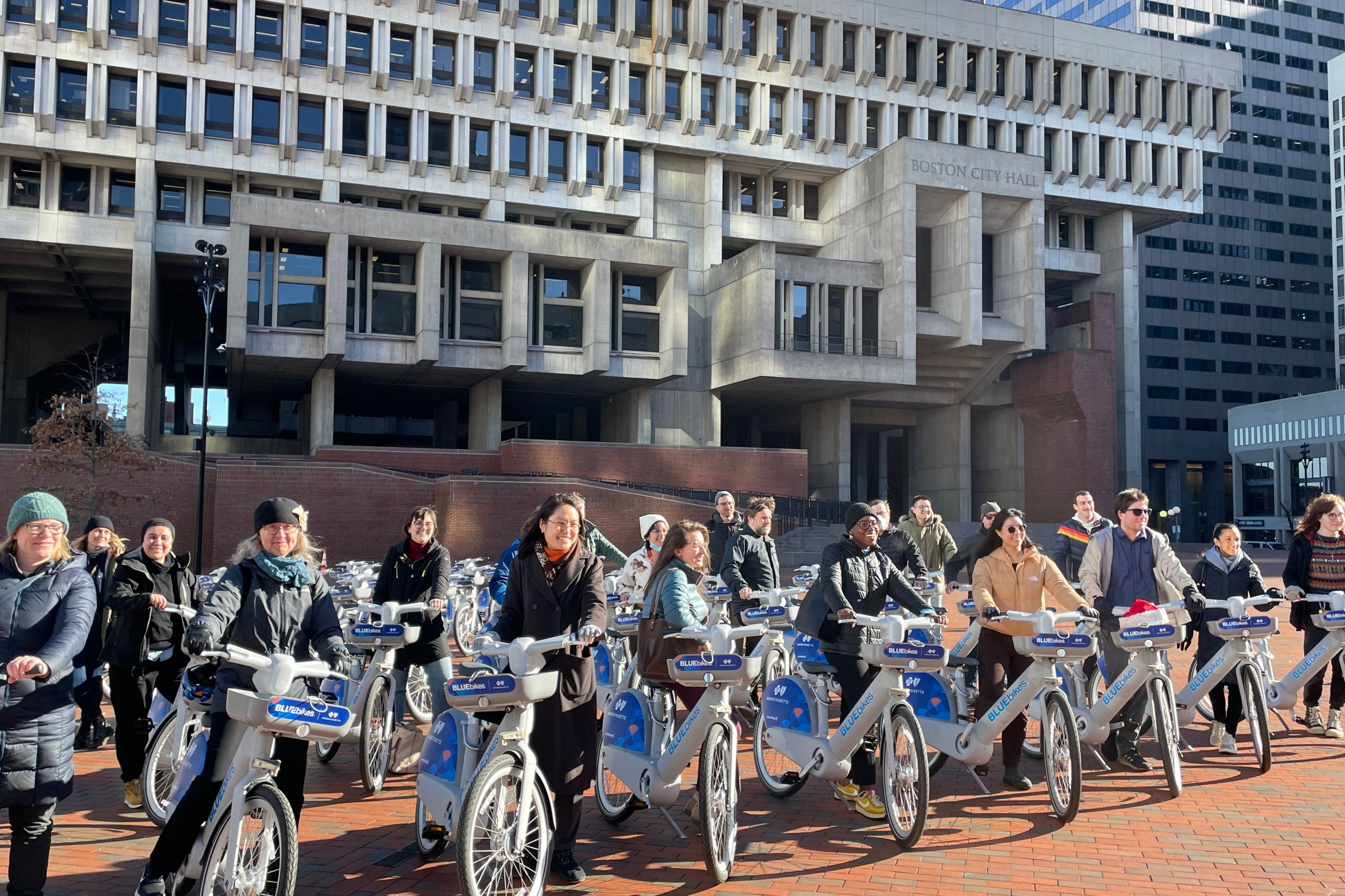 A crowd of people stand with new electric bikes in front of Boston City Hall