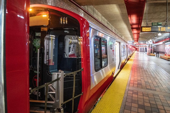 A new train with red trim waits at an empty subway platform.