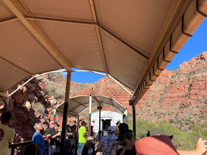 A covered, open-air train car full of passengers looking over Arizona red rocks in the Verde Valley.