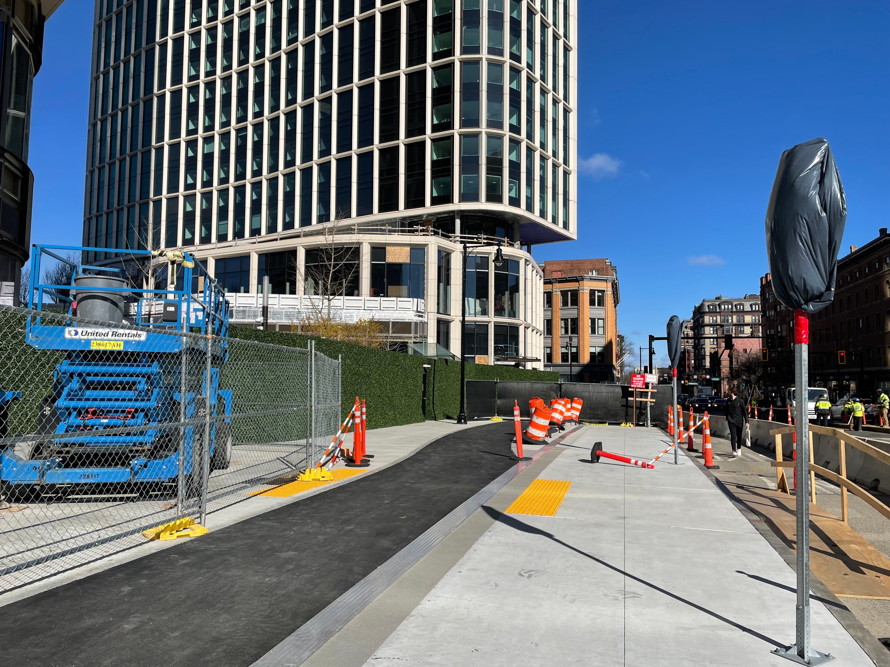 A sidewalk under construction with as asphalt bike path running down the middle. In the distance a new high-rise building rises behind a construction fence.
