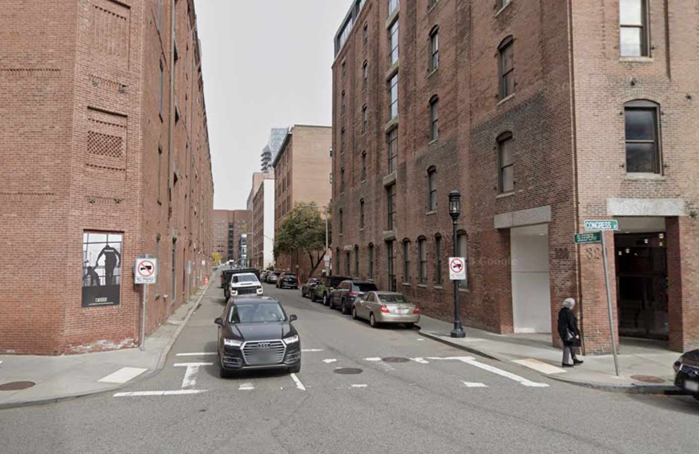 A narrow street lined with parked cars and mid-rise brick buildings.