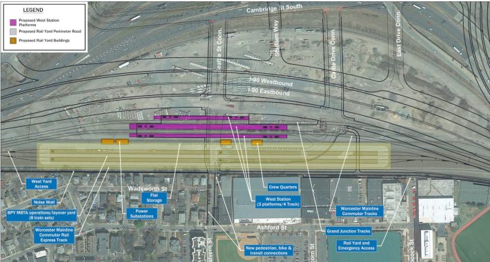 An aerial view of Allston near I-90 with outlines of planned infrastructure associated with the new West Station and new streets associated with a realigned Mass. Turnpike. A large yellow box in the center of the picture highlights a large area slated for a proposed train layover facility, just below to smaller purple rectangles that indicate proposed passenger platforms for a new train station.