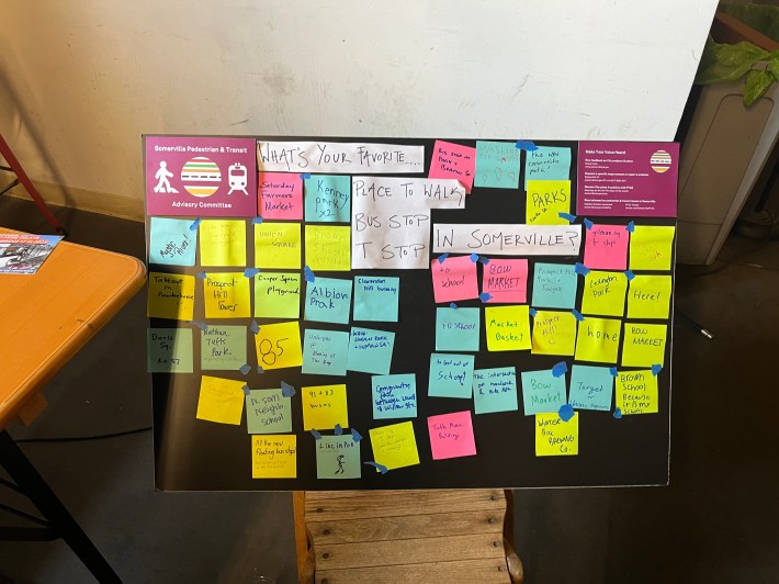 A black poster titled "What's your favorite place to walk, bus stop, T stop in Somerville?" filled with colorful sticky notes containing public comments on favorite places to walk and bus/subway stops.