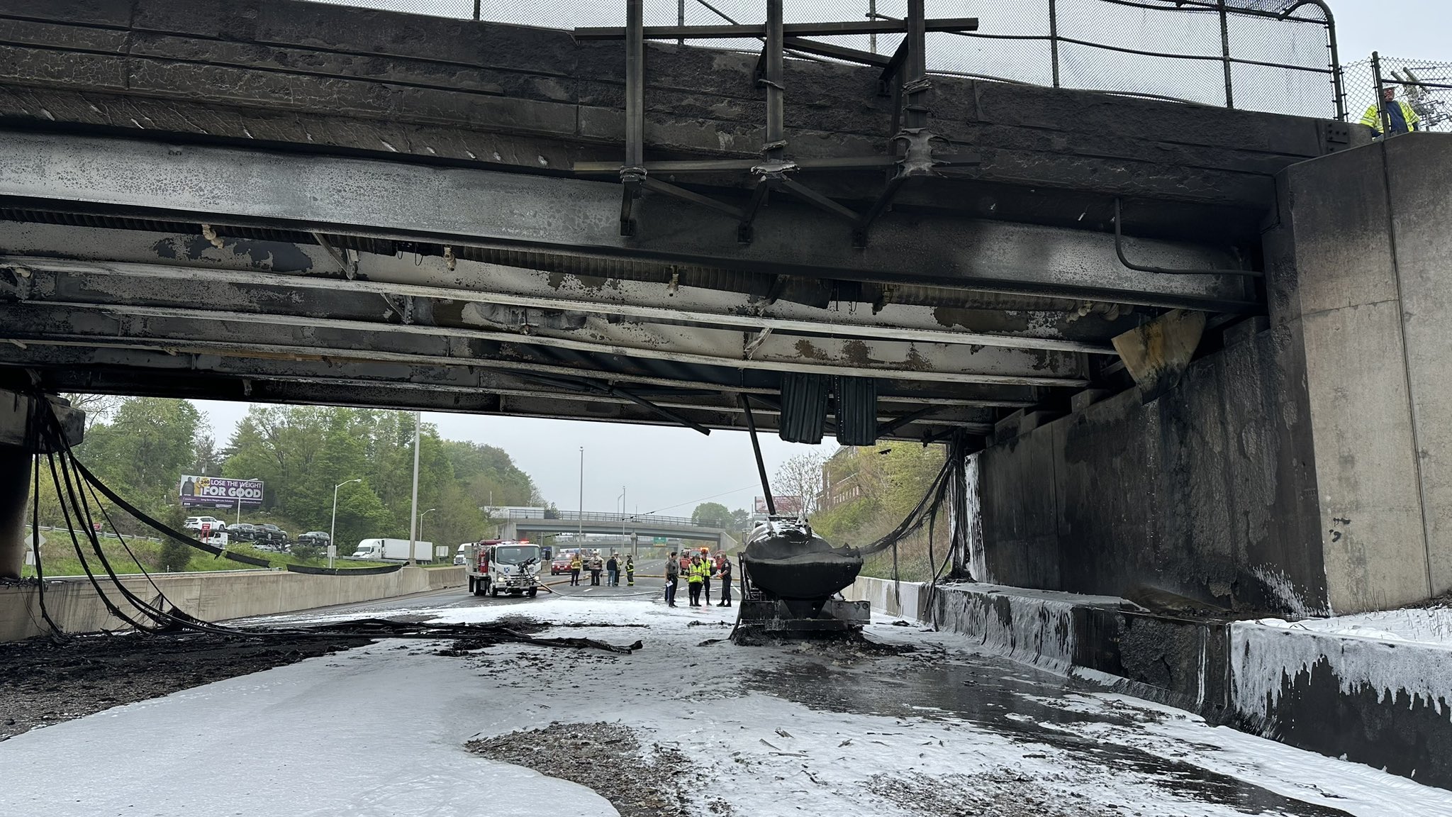 A burned-out highway overpass spans an empty highway covered in firefighting foam