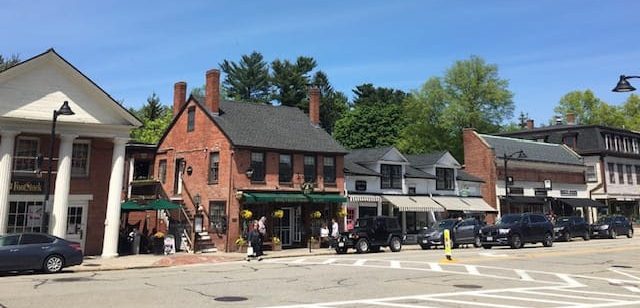 A row of 2-story brick buildings line a wide street with a crosswalk in the foreground.