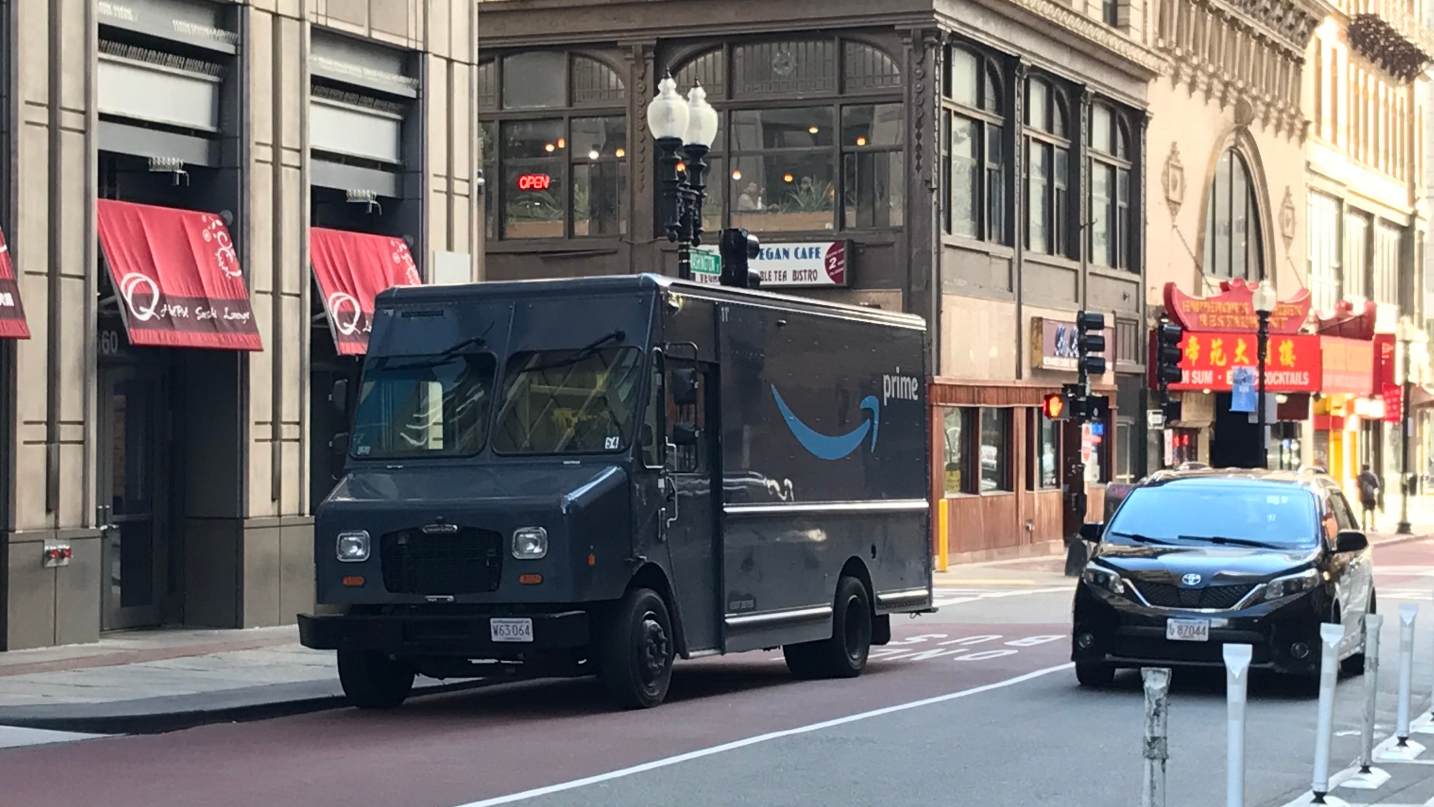 A blue Amazon delivery van parked illegally in a red dedicated bus lane next to a row of historic buildings along Washington Street in downtown Boston