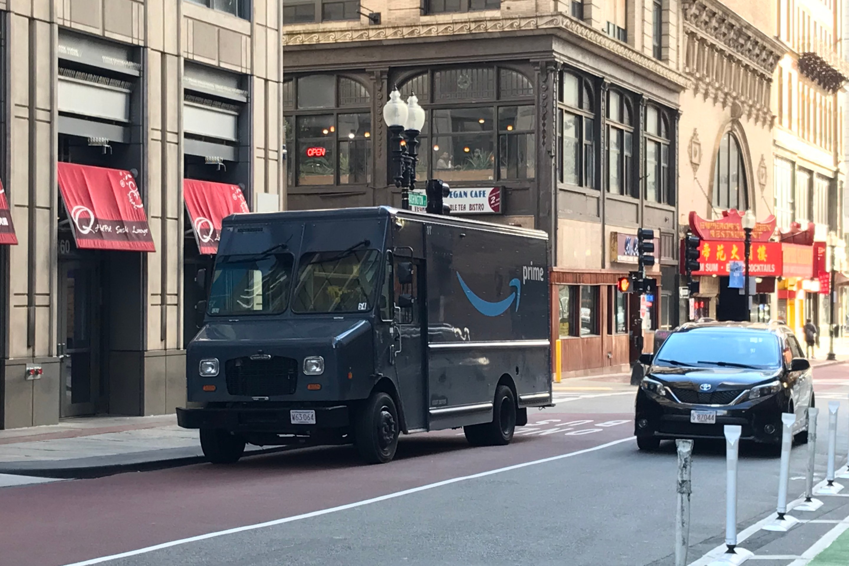 A blue Amazon delivery van parked illegally in a red dedicated bus lane next to a row of historic buildings along Washington Street in downtown Boston