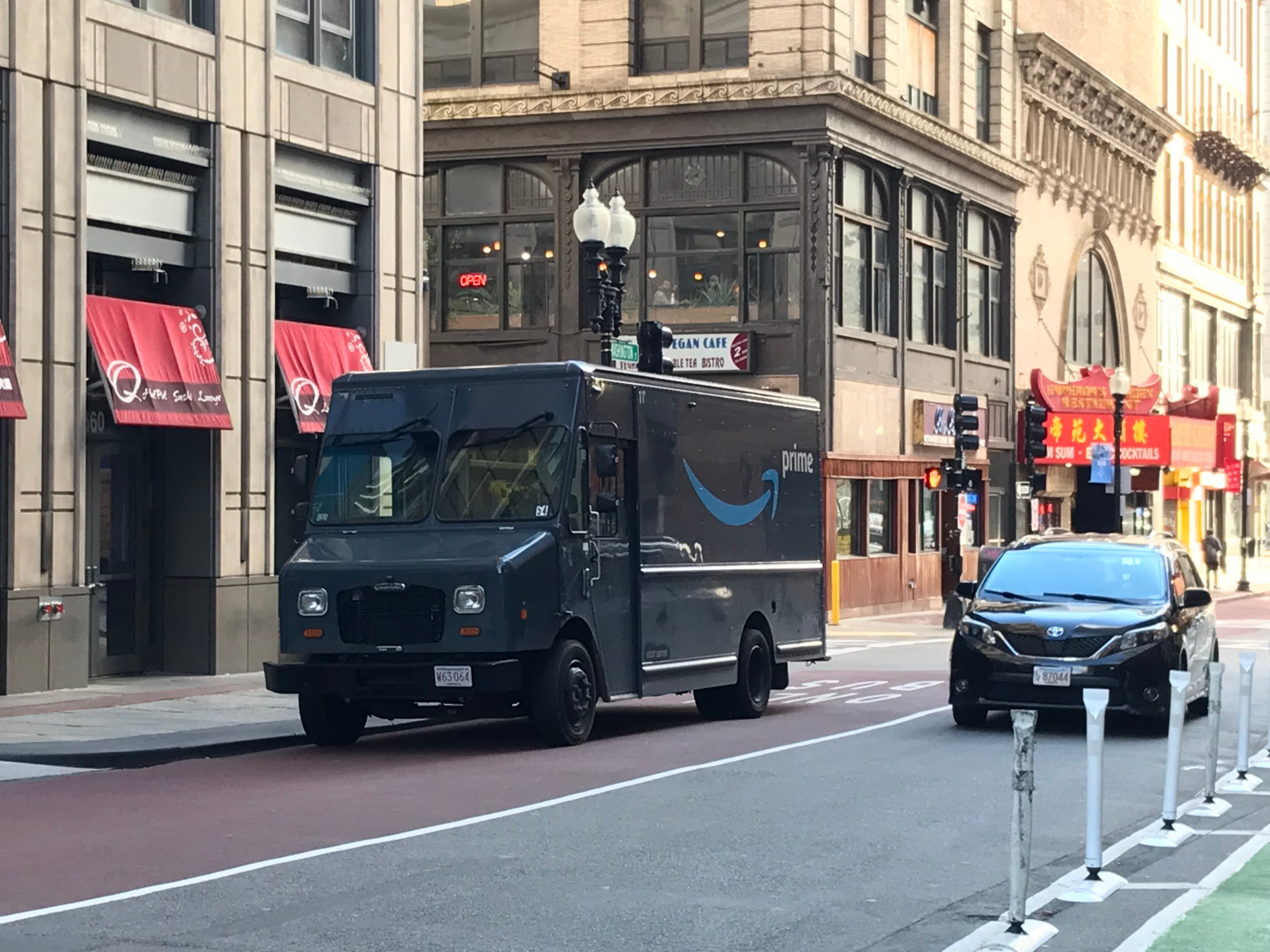 A blue Amazon delivery van parked illegally in a red dedicated bus lane next to a row of historic buildings along Washington Street in downtown Boston