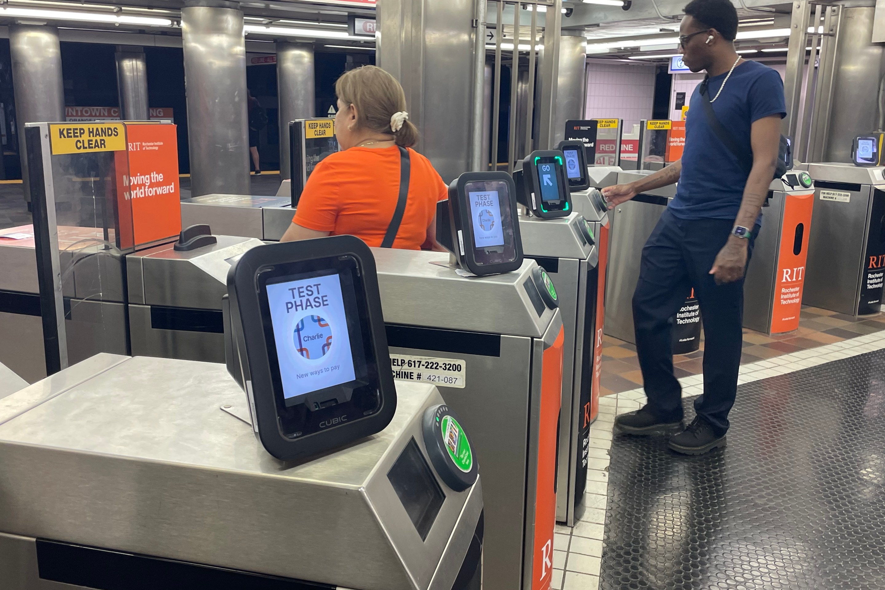 Two passengers pass through a row of fare gates at the Downtown Crossing MBTA station.