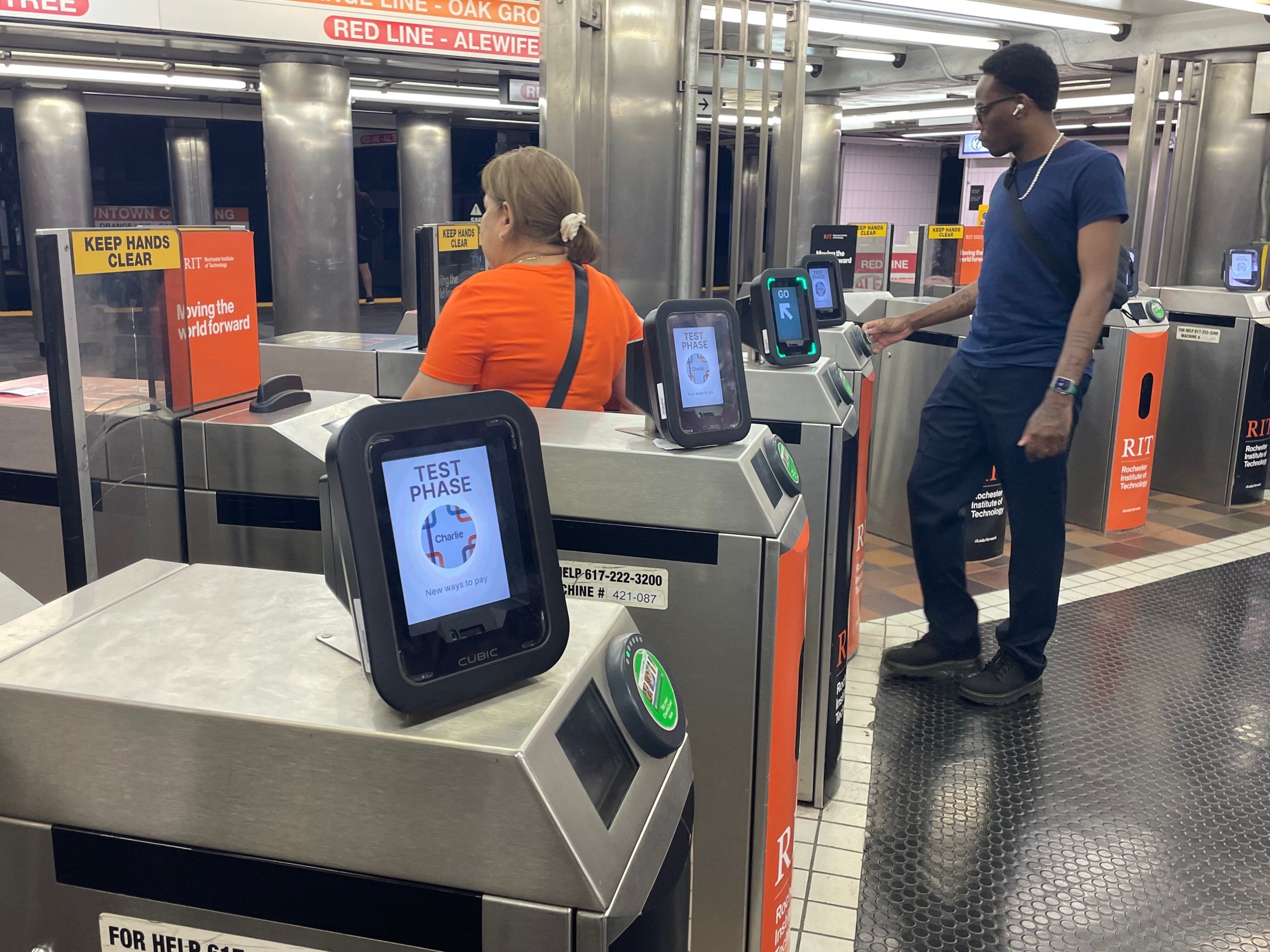 Two passengers pass through a row of fare gates at the Downtown Crossing MBTA station.