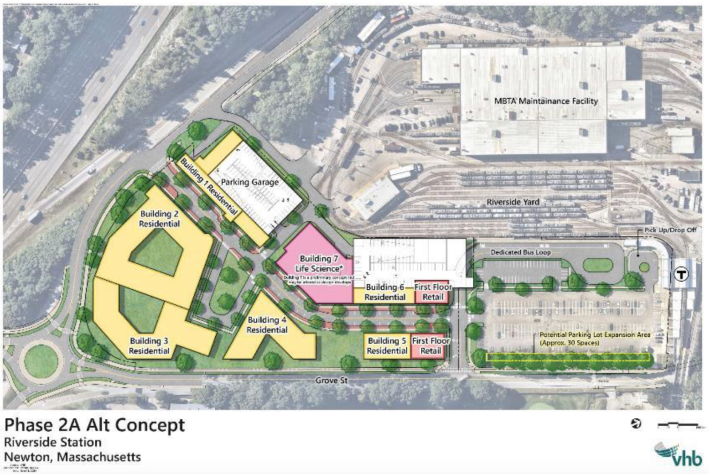 A birds-eye-view site plan for the proposed Phase 2 Riverside redevelopment. The image shows several residential buildings on the western edge of the site, plus two parking garages abutting the MBTA Green Line maintenance facility. An existing MBTA surface parking lot occupies the eastern edge of the side next to the Riverside MBTA station.