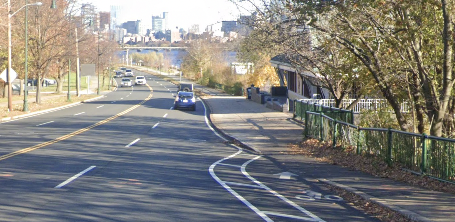 A four-lane roadway along a river. In the foreground a bike lane along the right side curb abruptly ends with an arrow pointing up onto a narrow sidewalk.