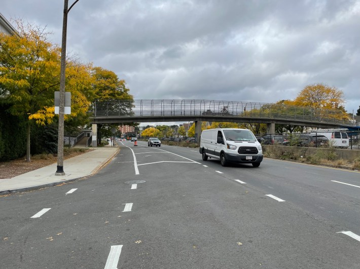 A wide highway with a fenced-in pedestrian overpass in the distance