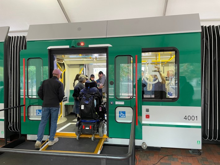 A person in a wheelchair uses a small ramp to cross the threshold of a MBTA Green Line train next to a window with a large wheelchair icon.
