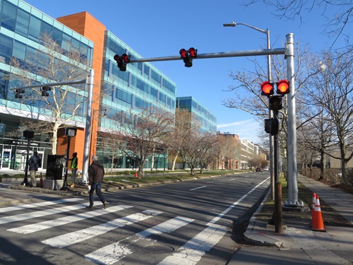 A set of red lights on a mast arm suspended over a crosswalk on a multi-lane city street