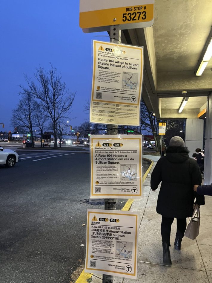 A photo of a pole with three signs displaying route change information for the MBTA bus network in English, Spanish, and Mandarin. The top sign, in English, announces changes to specific bus routes starting December 15, 2024, with a QR code for more information.