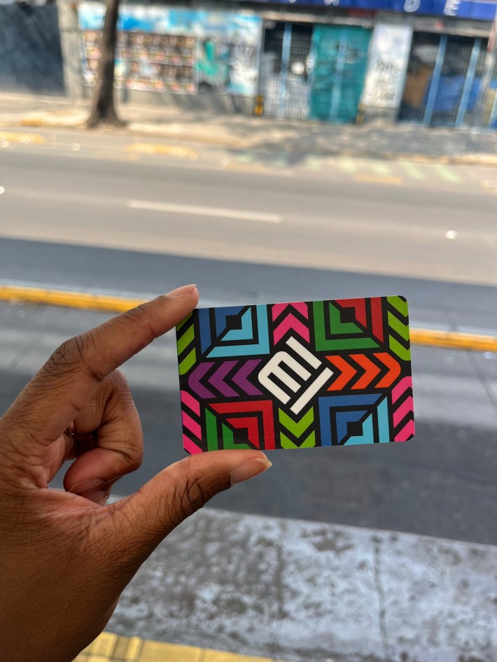 A close-up of Mexico City's metro card, which features a colorful grid of squares and diagonal lines surrounding the letters "MI" on a diagonal in the center of the card.