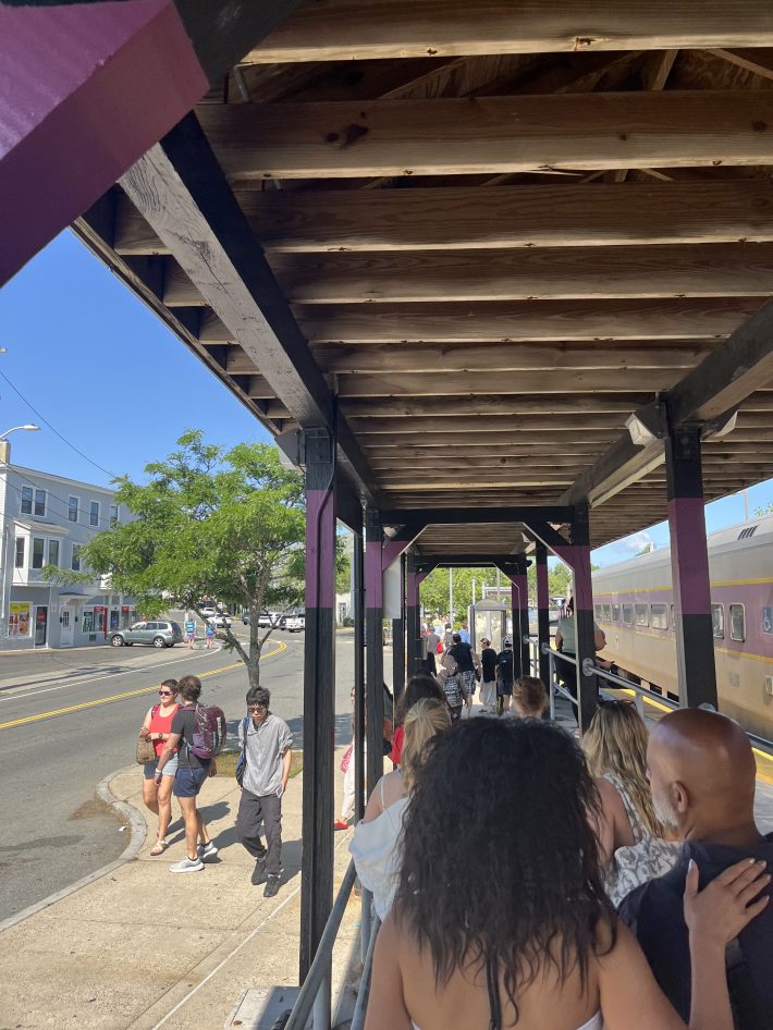 A crowd of people walking under a wooden canopy next to a departing commuter rail train.