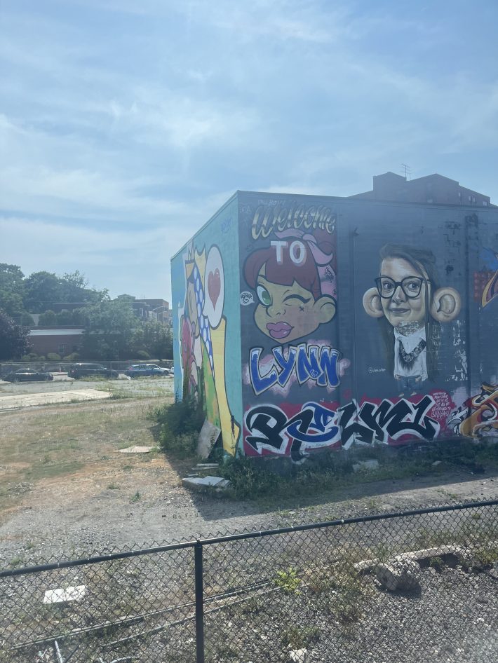 A colorful mural on the side of a building in Lynn, MA featuring cartoon-style faces with the words "Welcome to Lynn."