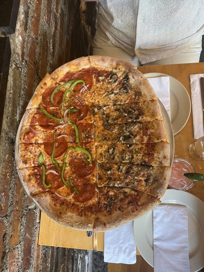 A large pizza divided into two sides. One side with mushrooms, the other with pepperoni, green peppers, and red onions, on a silver tray.