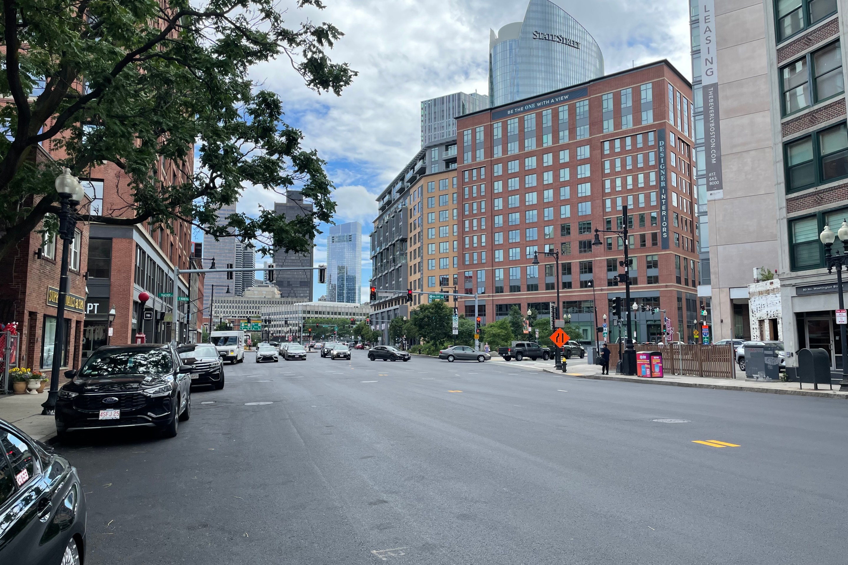 A wide city street with fresh asphalt and no painted lane markings. In the background are several high-rise buildings