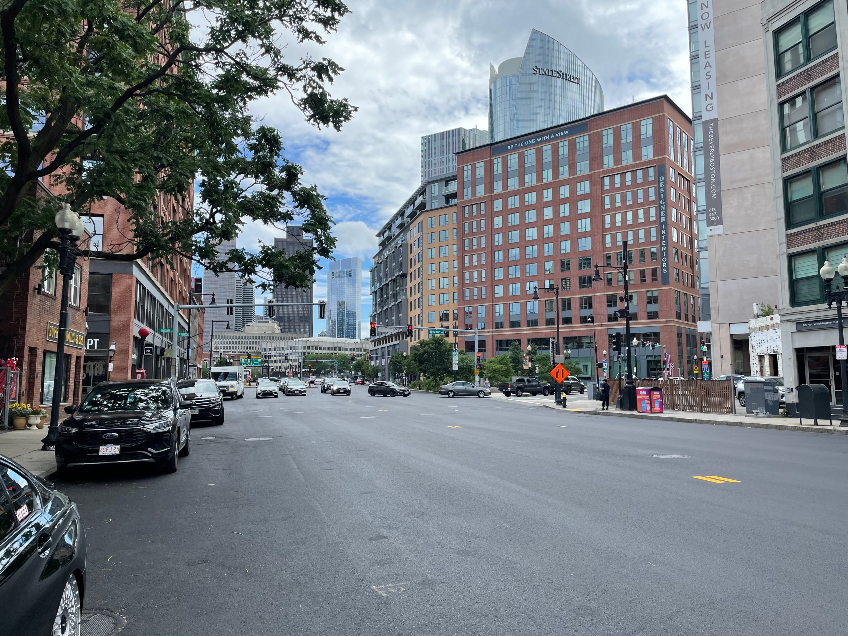 A wide city street with fresh asphalt and no painted lane markings. In the background are several high-rise buildings