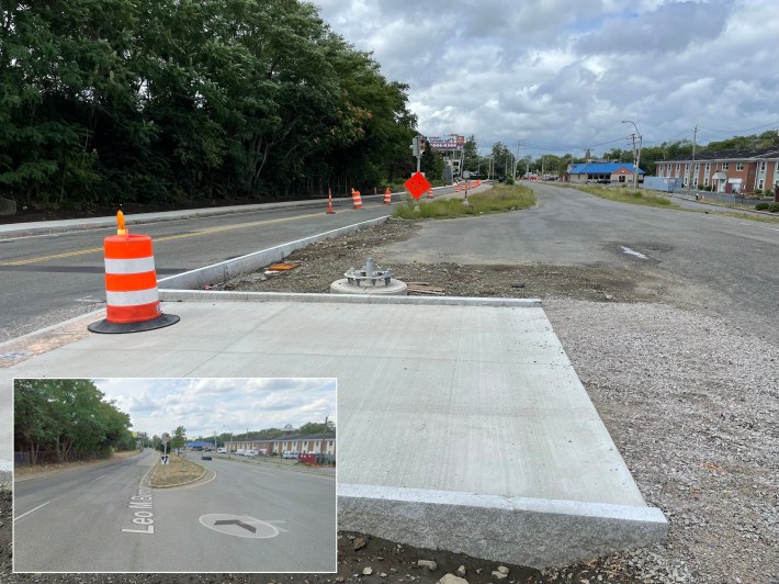 A highway construction site. New granite curbs have been installed in the middle of an older roadway with a run-down building with a blue-tiled roof visible in the distance to the right. Several orange construction barrels dot the roadway. An inset at lower left shows what the same scene looked like before construction, when the same view showed a wide field of asphalt connecting an otherwise divided four-lane highway.