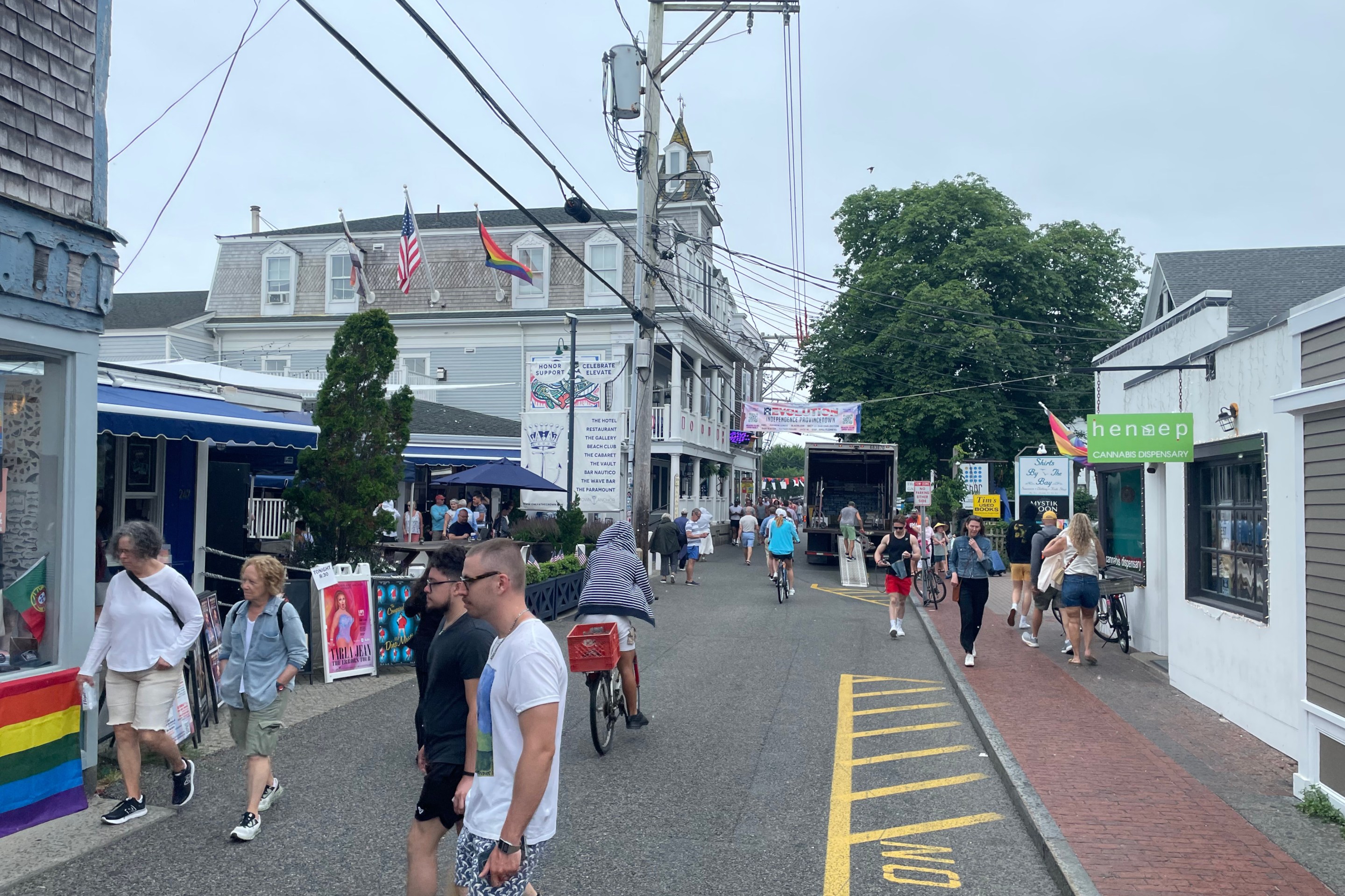 Pedestrians fill a narrow street lined with two-and three-story retail buildings. There's a narrow brick sidewalk on the right edge of the street.