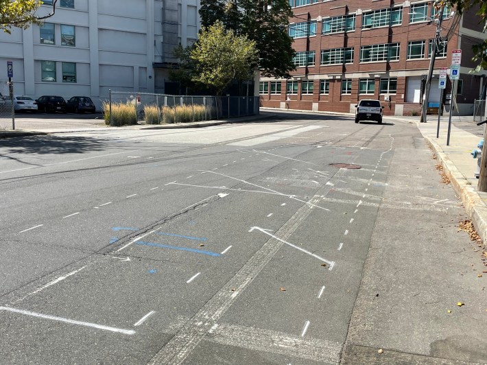 Spray-painted white lines mark out future lane markings on a city street with patchy asphalt pavement.