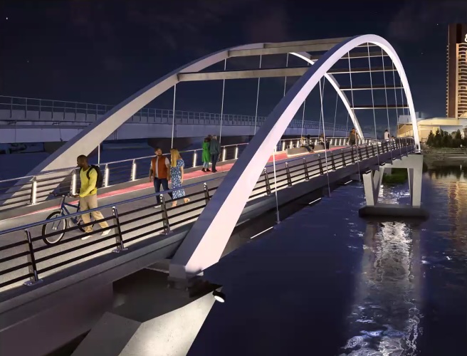 A rendering of an arched bridge lit up at night over a river with a high-rise glass building on the horizon in the upper right corner. The bridge has no cars and a handful of pedestrians are pictured walking along its surface, which is about 18 feet wide, between two waist-high railings.