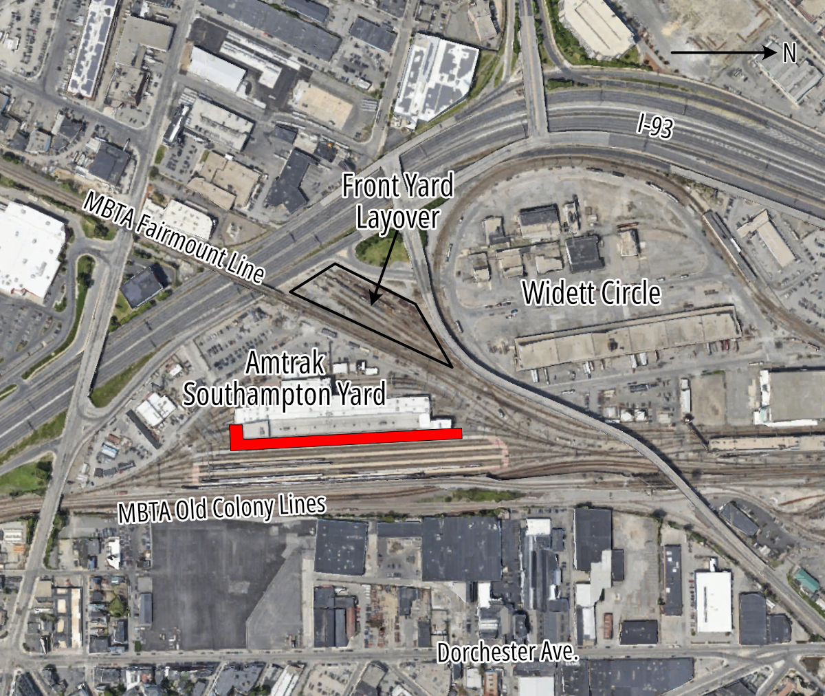 An aerial view of railyards in South Boston. Interstate 93 curves through the image from the left center to the upper right. North is to the right. The MBTA Red Line and Old Colony Lines cross the image horizontally near the bottom. The MBTA Fairmount Line crosses diagonally, from the upper left corner, to meet the Old Colony tracks at lower right. The planned Widett Circle layover facility is in the right center of the image, inside the curve of I-93. In the left center is a the Amtrak Southampton Yard facility, which includes a large indoor maintenance facility. A red rectangle beneath the existing facility indicates the area where the facility will be expanded.