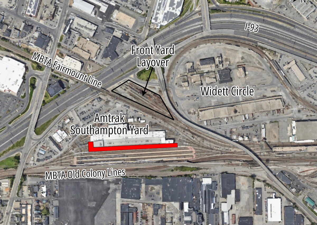 An aerial view of railyards in South Boston. Interstate 93 curves through the image from the left center to the upper right. North is to the right. The MBTA Red Line and Old Colony Lines cross the image horizontally near the bottom. The MBTA Fairmount Line crosses diagonally, from the upper left corner, to meet the Old Colony tracks at lower right. The planned Widett Circle layover facility is in the right center of the image, inside the curve of I-93. In the left center is a the Amtrak Southampton Yard facility, which includes a large indoor maintenance facility. A red rectangle beneath the existing facility indicates the area where the facility will be expanded.