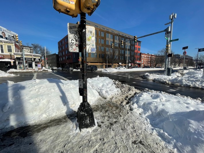A city intersection in winter, with its crosswalks blocked by high snowbanks.