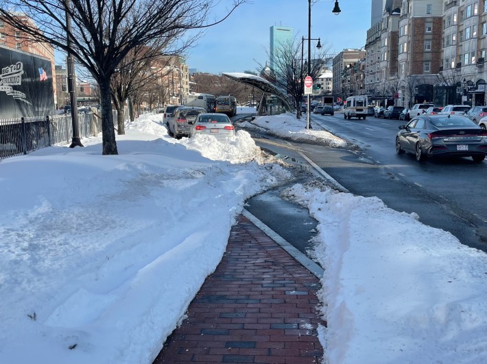 A poorly plowed walkway leads toward a bus stop in the middle of a wide city square.