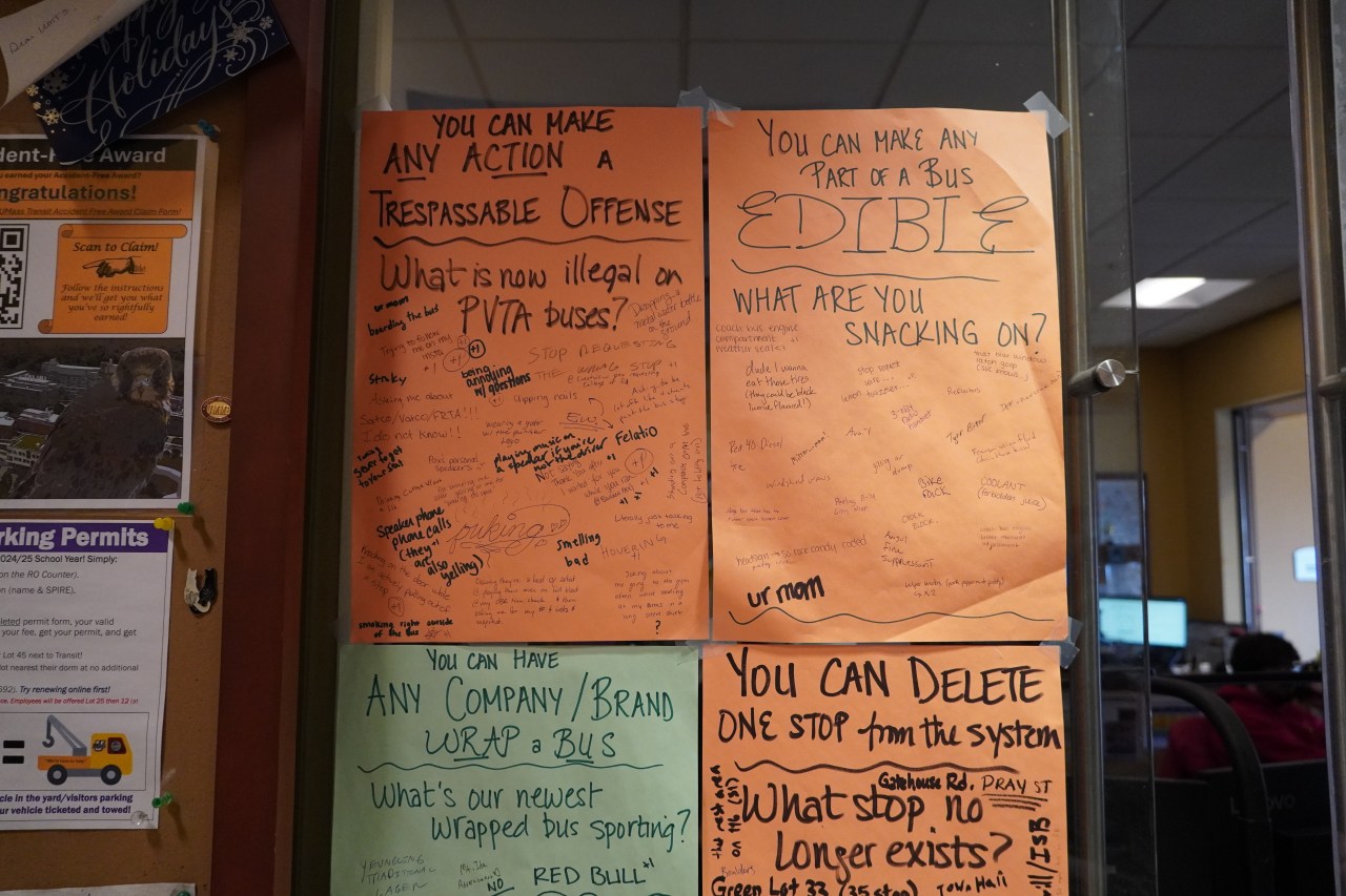 Posters hung from a wall on colorful paper, filled with handwriting from different people. The poster in the upper left is titled "What is now illegal on PVTA buses" with responses like "smelling bad," "being annoying with questions" and "trying to follow me on my insta." The upper right poster reads "you can make any part of a bus edible, what are you snacking on?" with responses like "red 40 diesel," "chock block" and "ur mom"